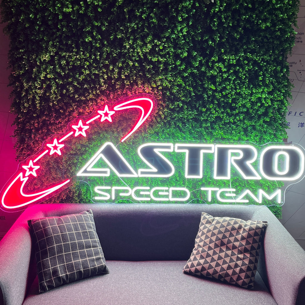 Neon sign of Astro Speed Team above a gray sofa with decorative pillows.